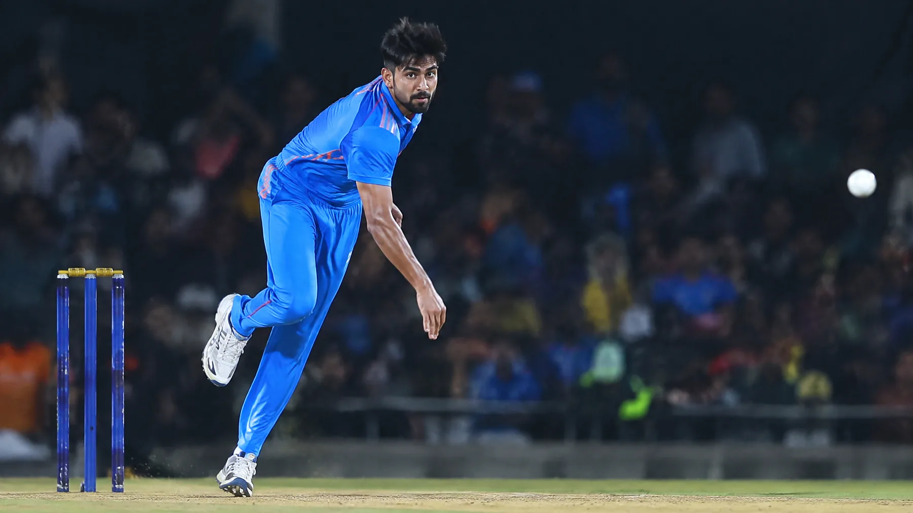 A fast bowler delivering under stadium lights